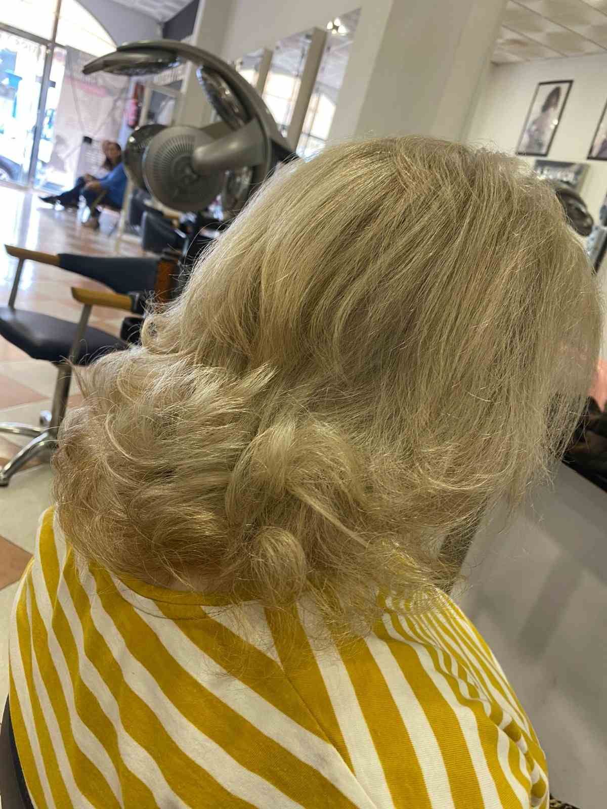 Cabello rubio peinado en capas sueltas en una peluquería, con una capa a rayas amarillas y blancas visible.