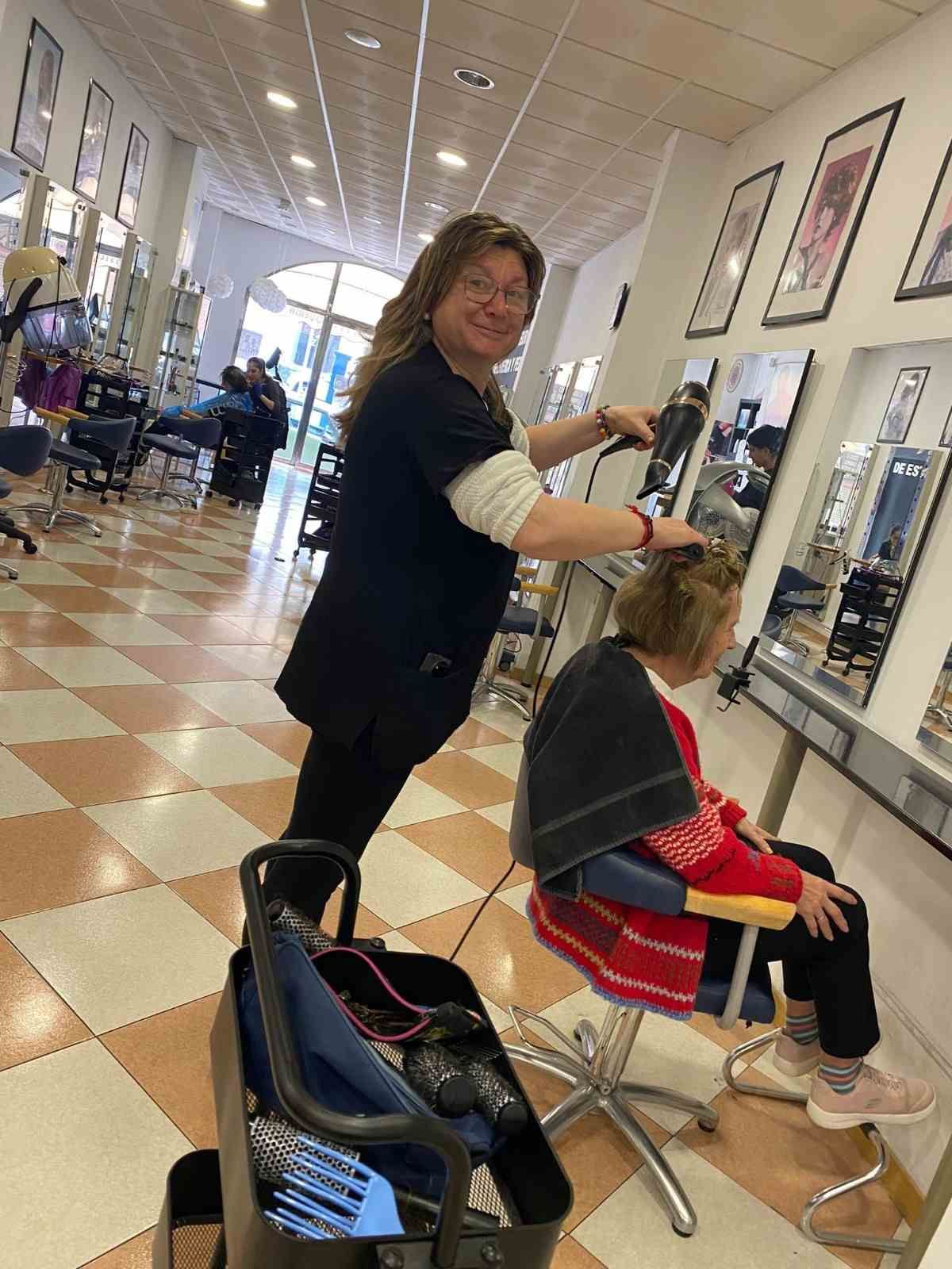 Estilista cortando el pelo en un salón luminoso con suelo de baldosas a cuadros y espejos enmarcados.