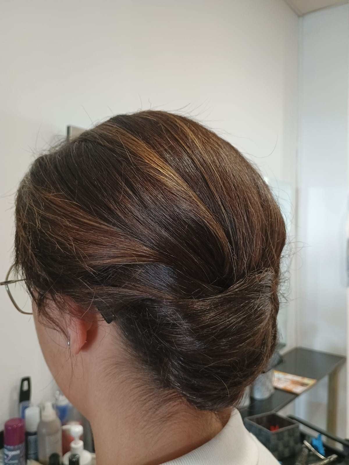 Vista posterior de un moño de cabello castaño con un giro trenzado, en una habitación con un espejo de tocador.