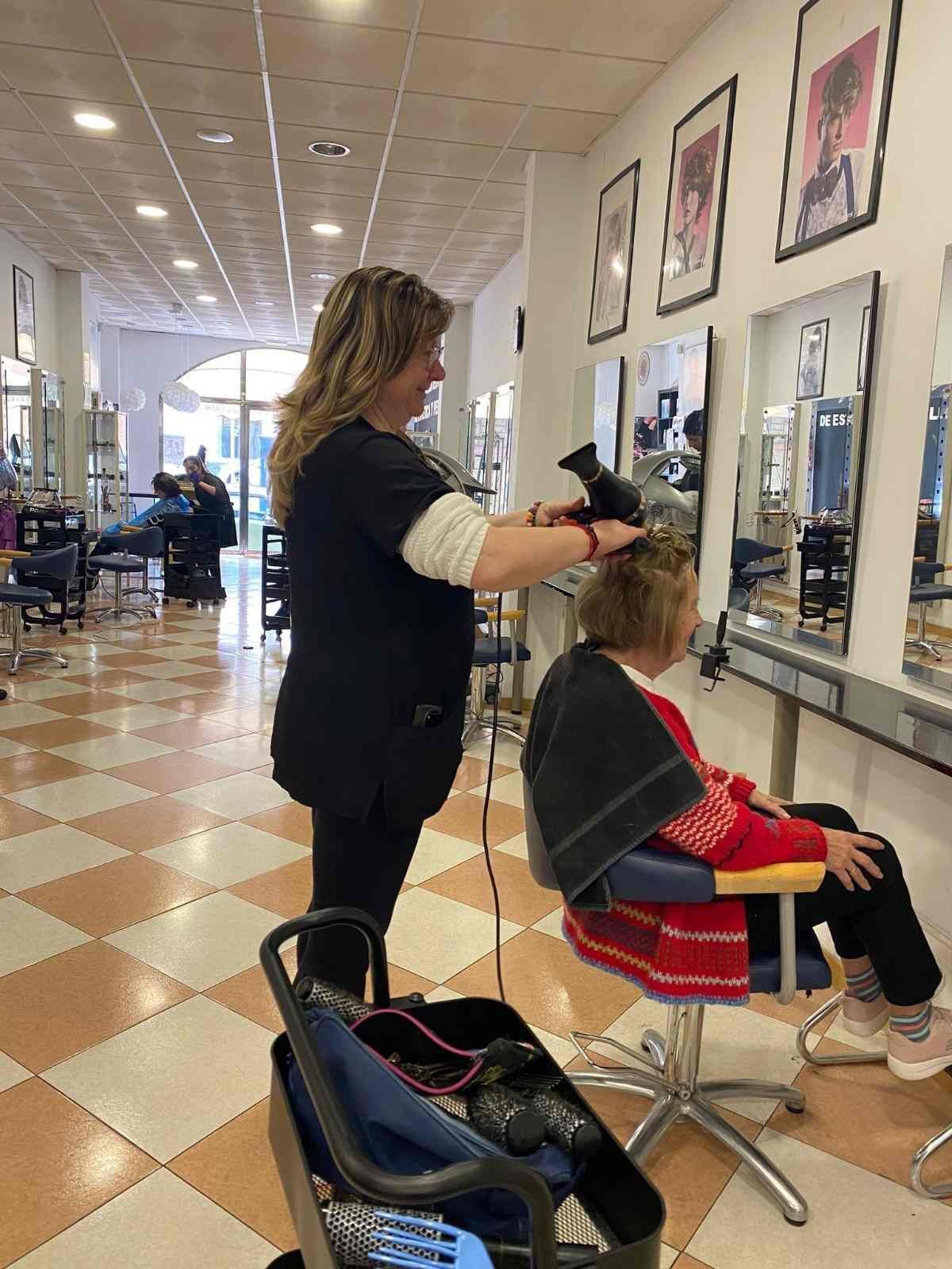 Peluquera cortando el pelo a una clienta en un salón con espejos y suelo de baldosas a cuadros blancas y negras.