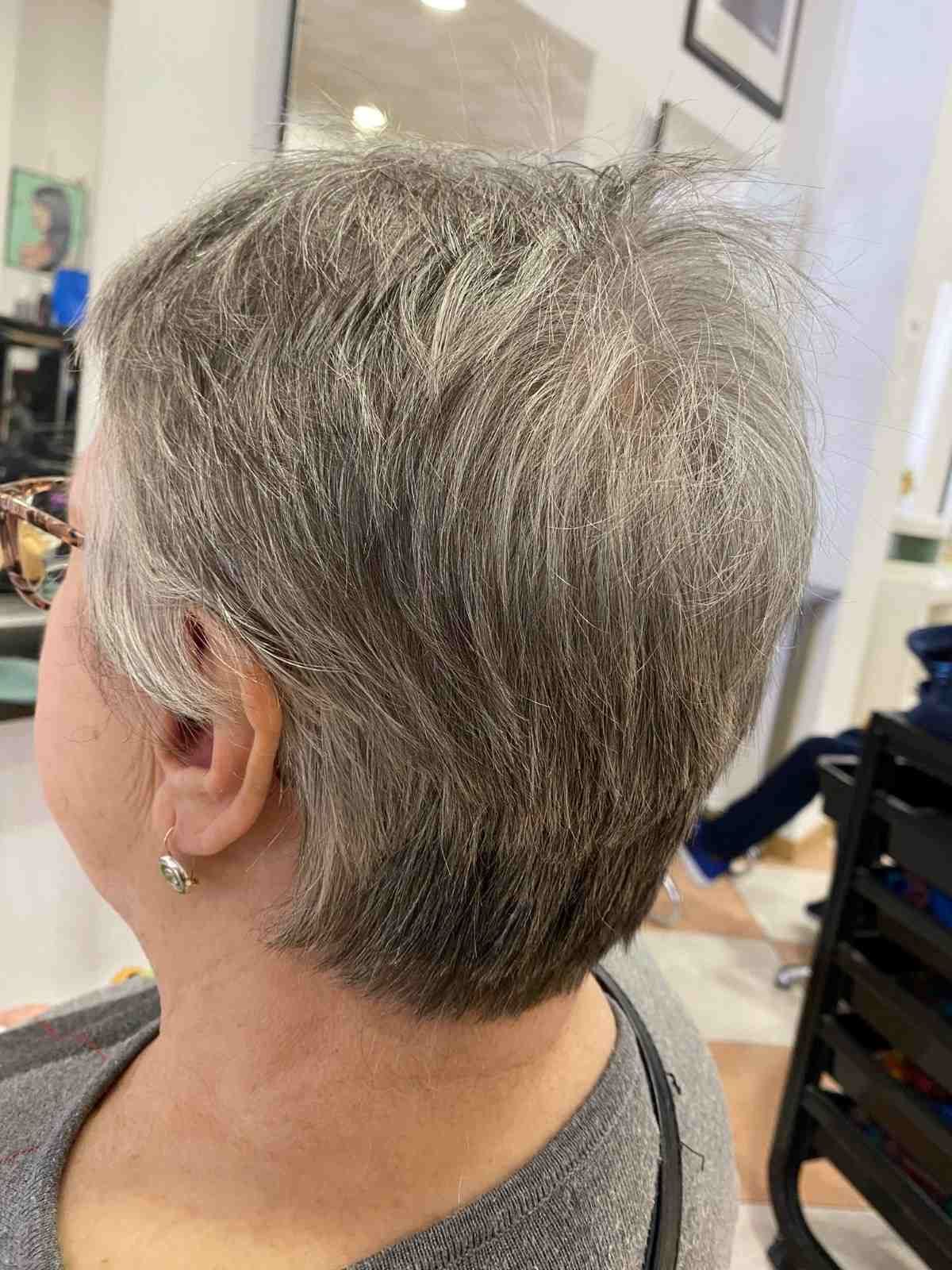 Corte de pelo pixie corto y gris visto de perfil y por detrás en una silla de peluquería.