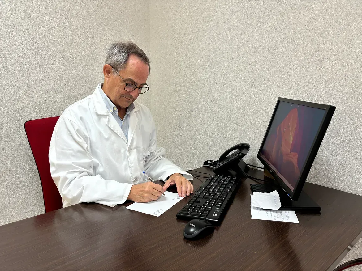 Un médico está sentado en un escritorio frente a una computadora.