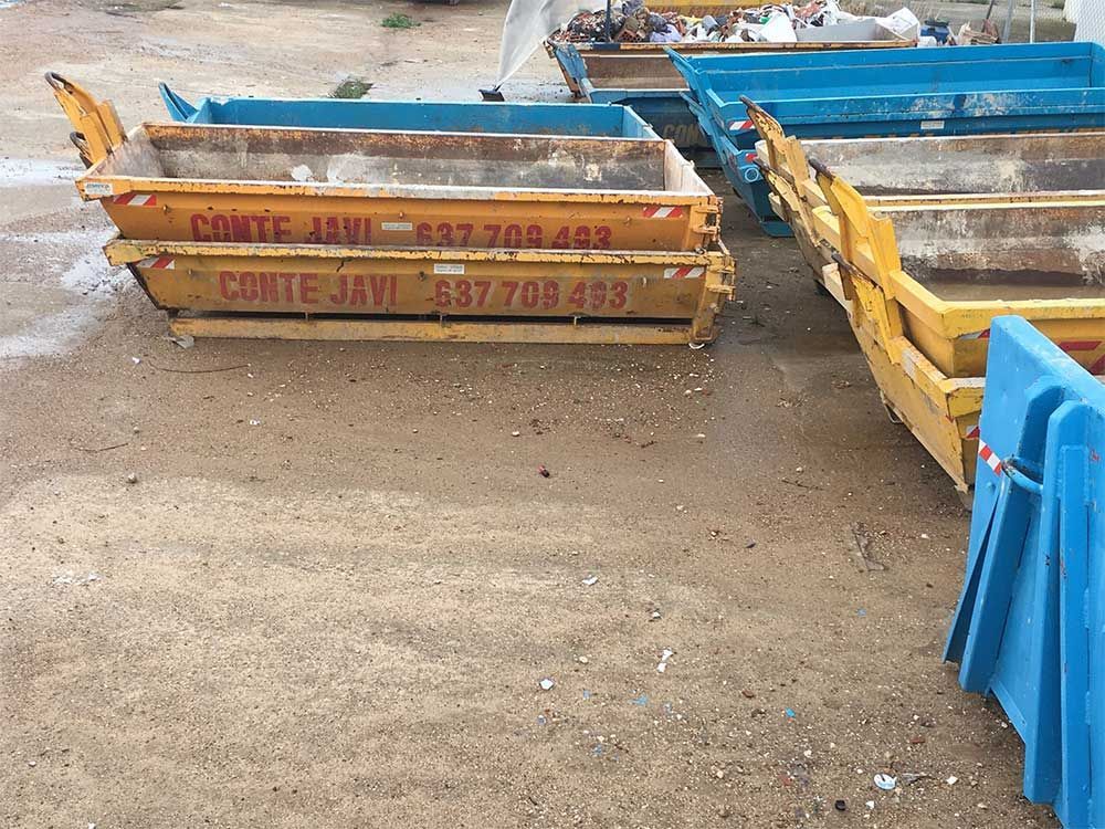 Contenedores industriales de color amarillo y azul apilados y alineados al aire libre sobre una superficie de tierra.