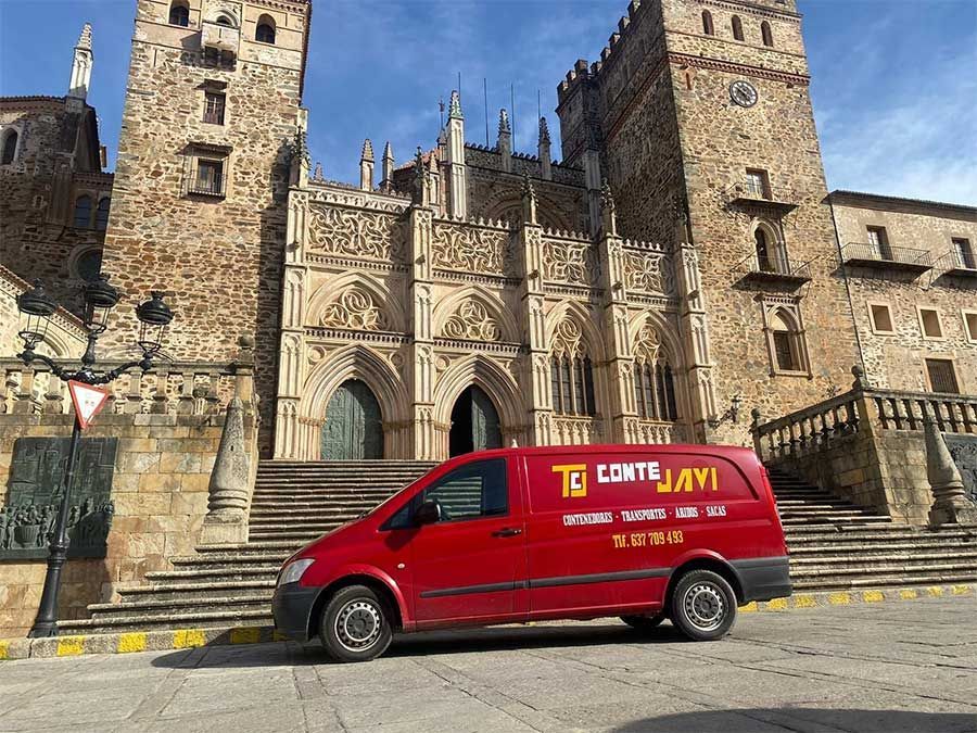 Furgoneta roja estacionada frente a una catedral de piedra con una gran puerta y escalones.