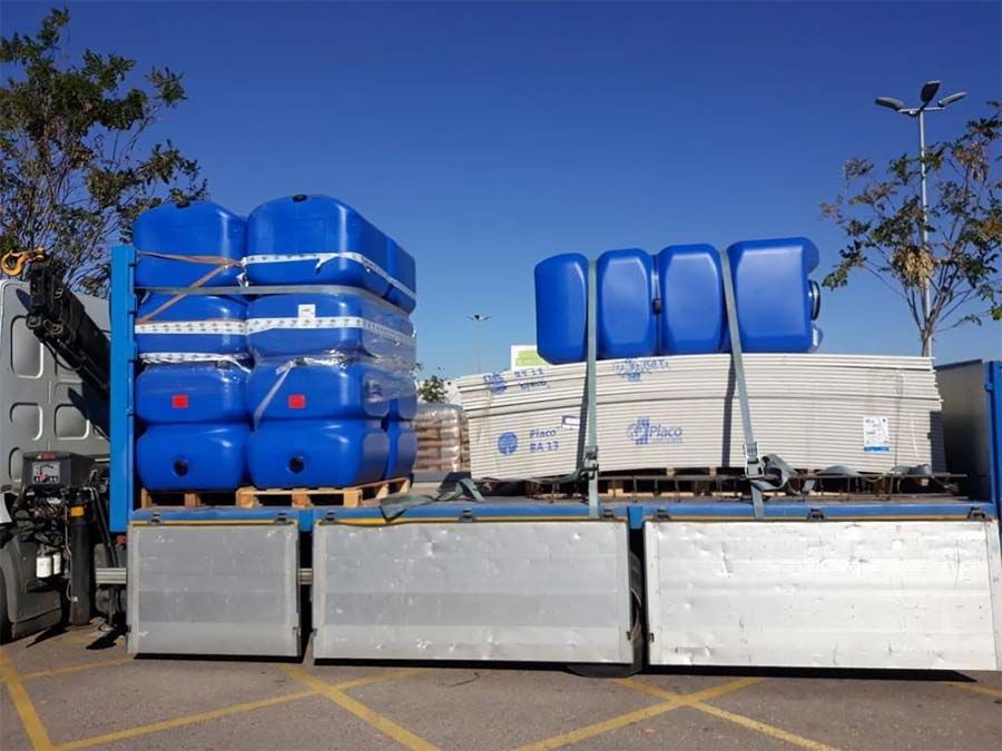Caja de camión cargada con tanques azules, paletas de artículos blancos y un cielo azul claro.