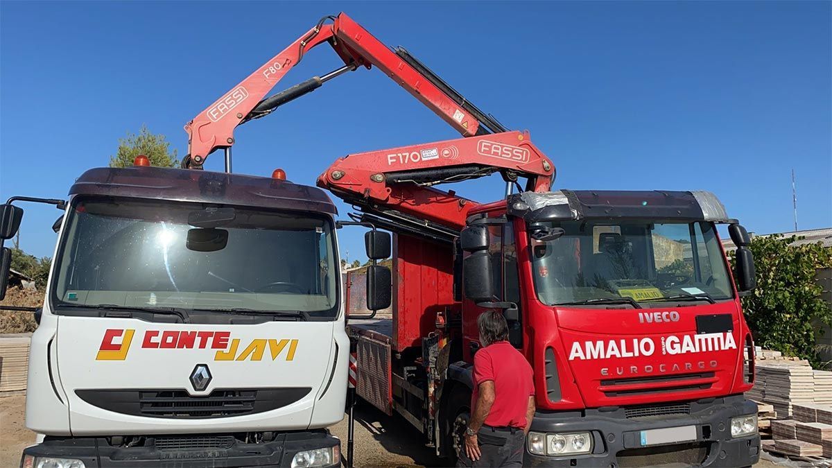 Dos camiones de trabajo con brazos grúa extendidos, uno rojo y otro blanco, al aire libre.