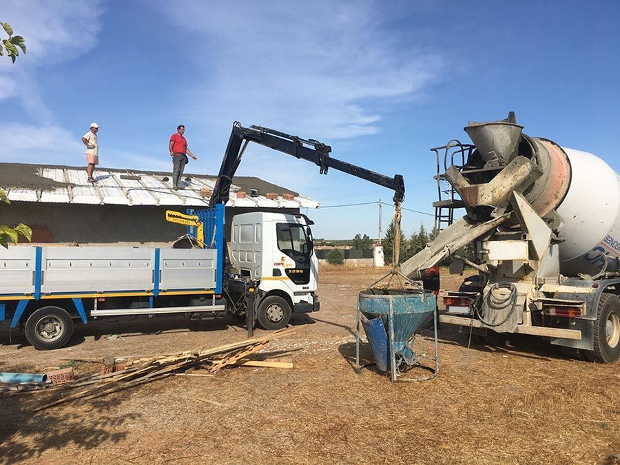 Camión con grúa entrega hormigón al techo donde dos trabajadores se encuentran bajo un cielo azul.
