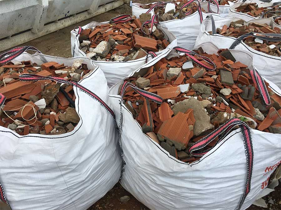 Bolsas blancas llenas de ladrillos rojos rotos y escombros, probablemente restos de construcción.