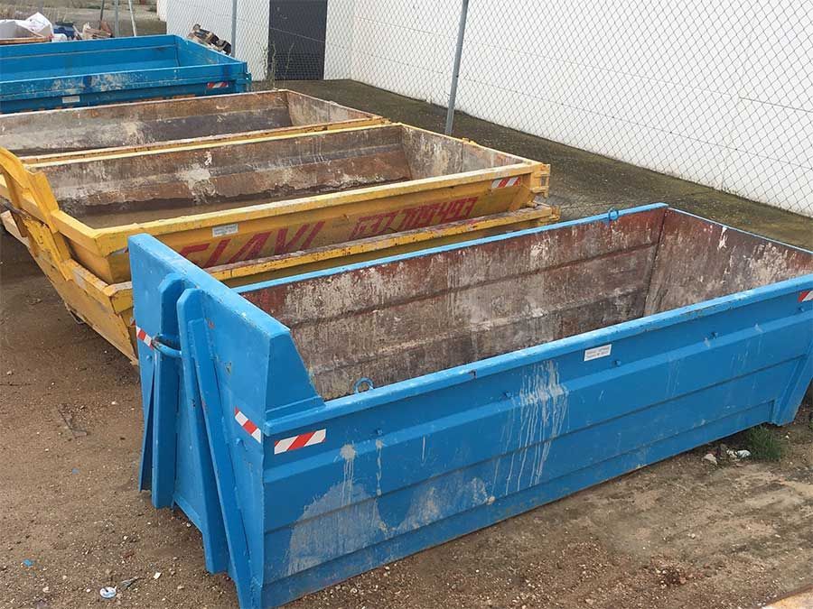 Contenedores rectangulares de color azul, amarillo y azul, uno al lado del otro sobre una superficie pavimentada.