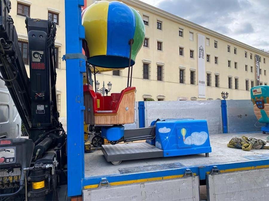 Un colorido paseo en globo aerostático sobre un camión de plataforma, cerca de un edificio beige.