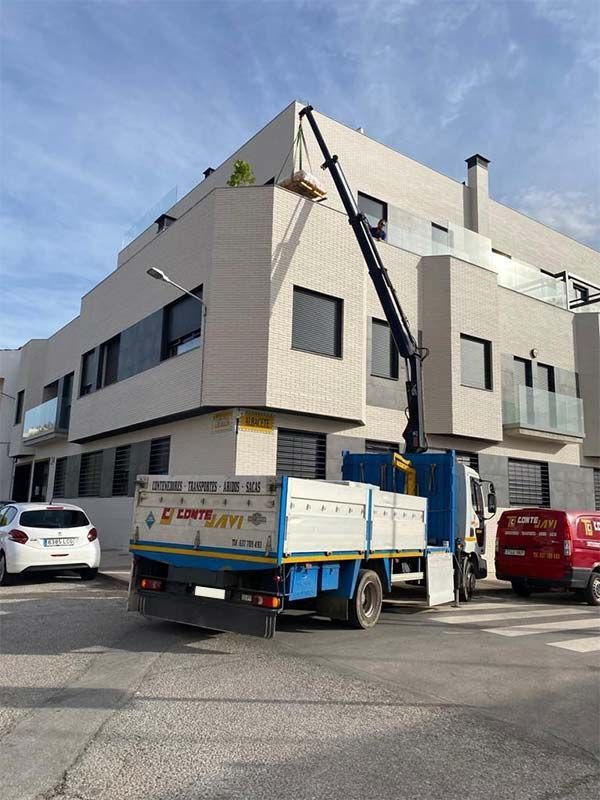 Camión grúa colocando un árbol en el tejado de un edificio blanco.