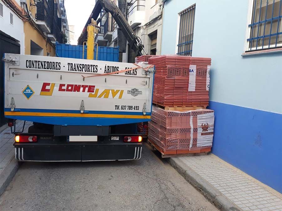 Camión descargando ladrillos en un callejón estrecho; el camión es blanco, azul y amarillo.