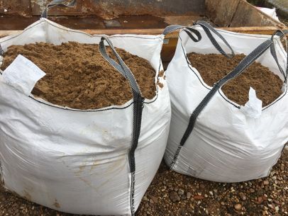 Dos grandes bolsas blancas llenas de arena marrón, al aire libre.