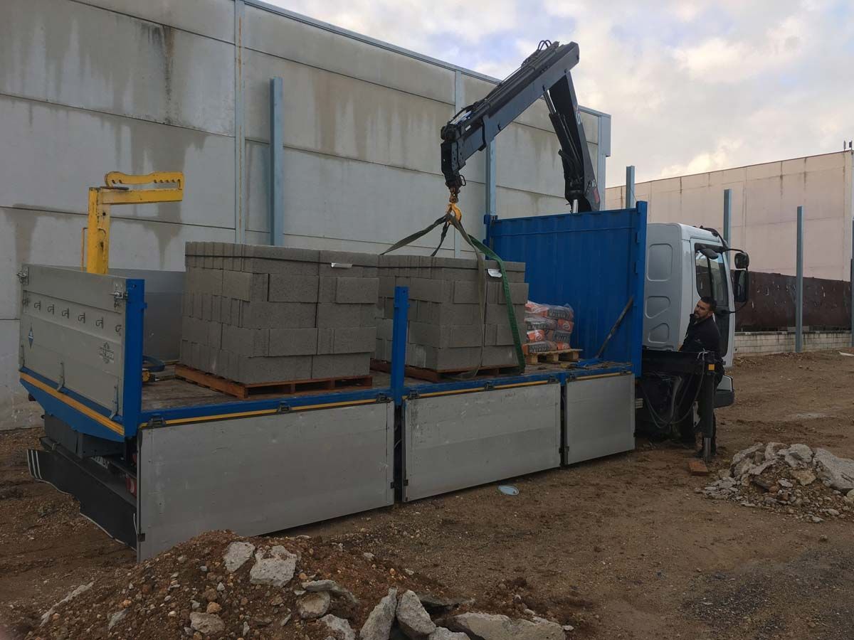 Camión con grúa cargando bloques de hormigón. Un trabajador se encuentra cerca, en una obra de construcción.