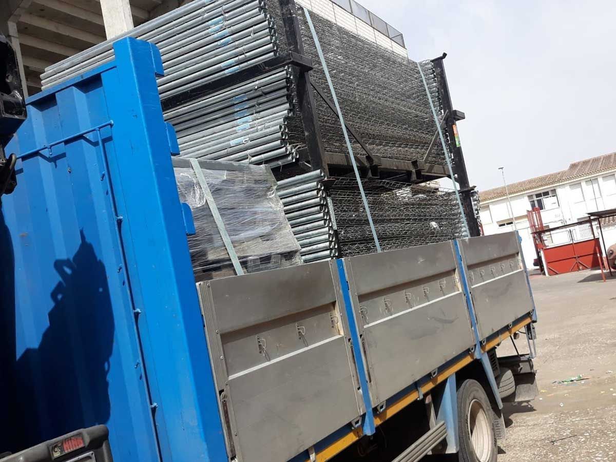 Camión azul con andamios metálicos en la parte trasera. A la intemperie, soleado.