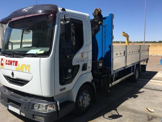 Camión Renault de color blanco con grúa y plataforma de color azul, estacionado al aire libre.