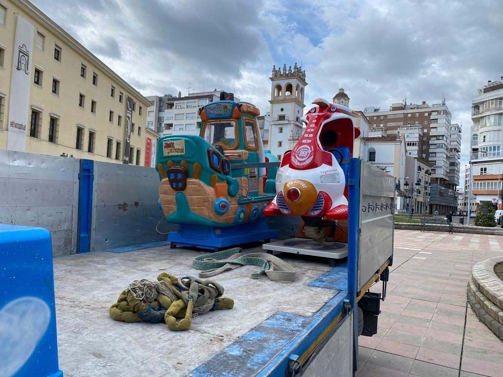 Una caja de camión con dos atracciones infantiles: un barco y un cohete, estacionada en una plaza de la ciudad.