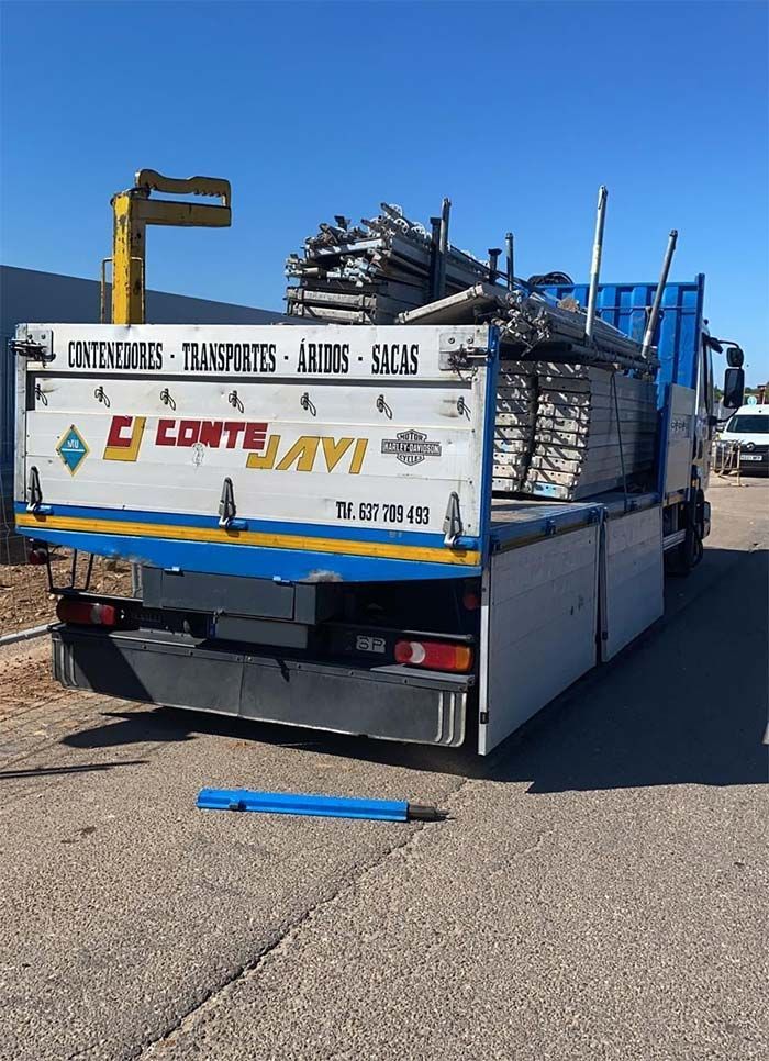 Caja de camión cargada con andamios metálicos contra un cielo azul, logo 
