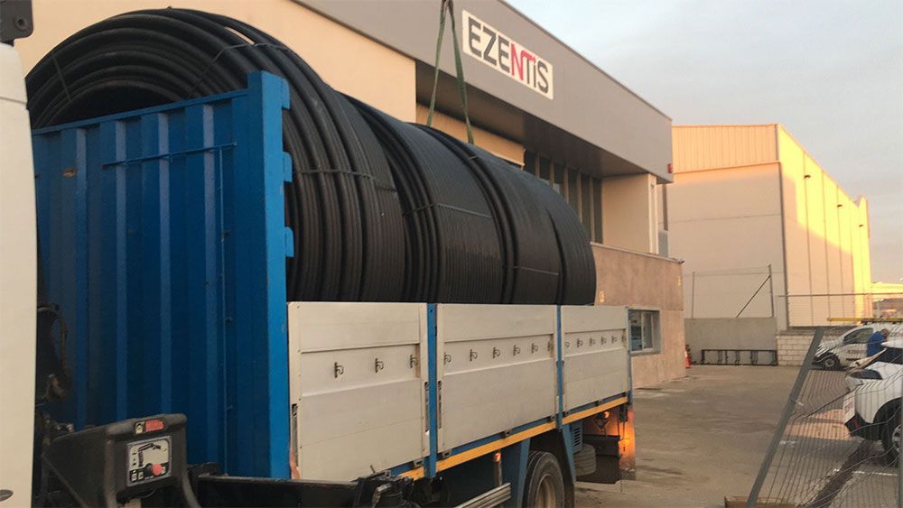 Camión cargado con grandes tubos negros frente a un edificio con 