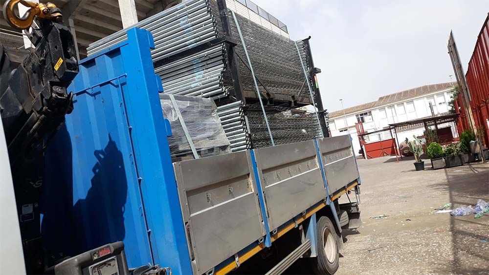 Camión azul cargado con tubos de andamios metálicos en un entorno al aire libre.