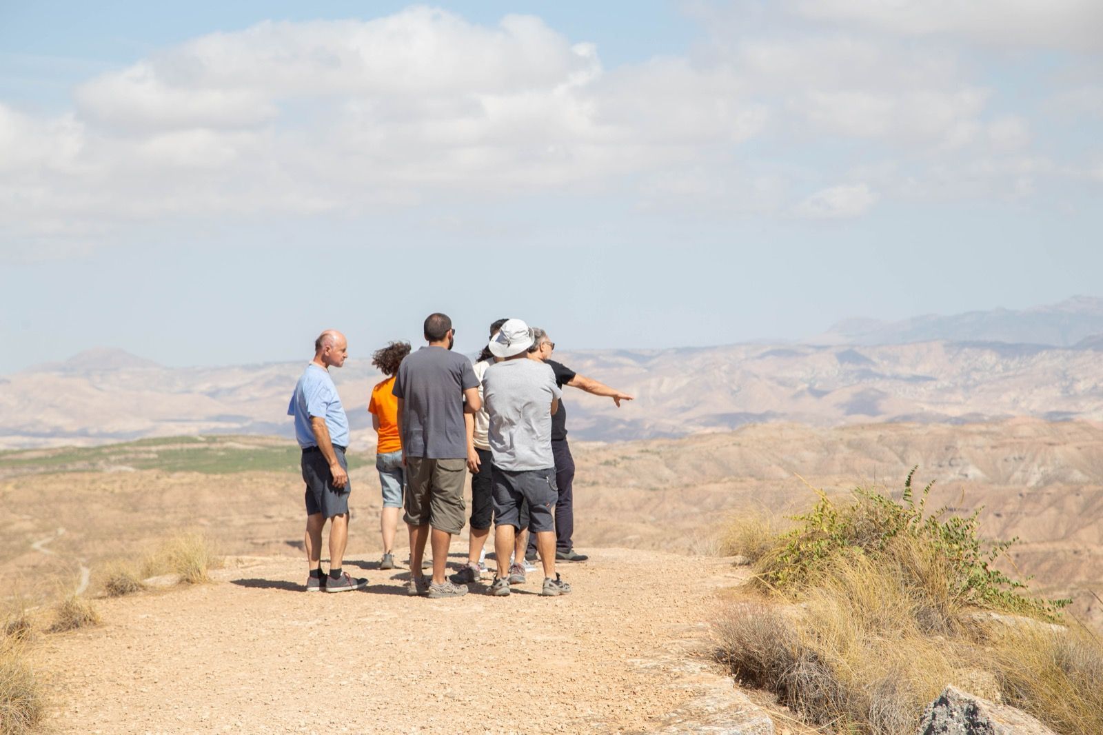 Un grupo de personas está de pie en la parte superior de un camino de tierra mirando el paisaje.
