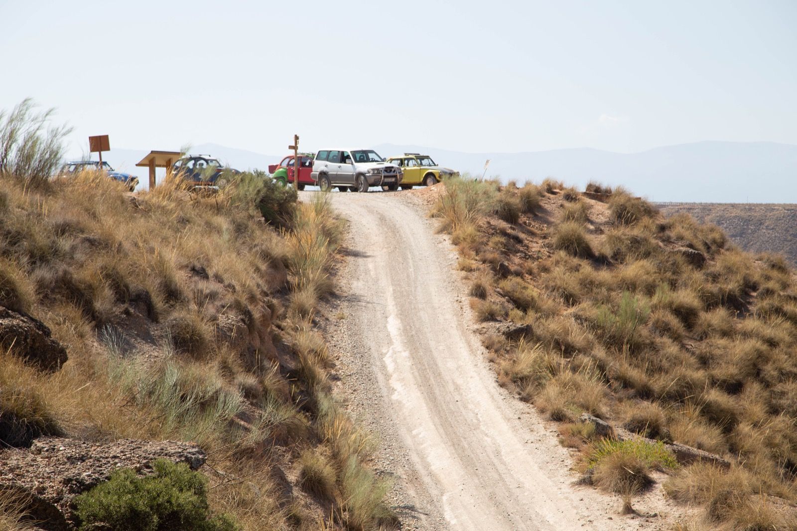 Un grupo de coches están estacionados al costado de un camino de tierra.