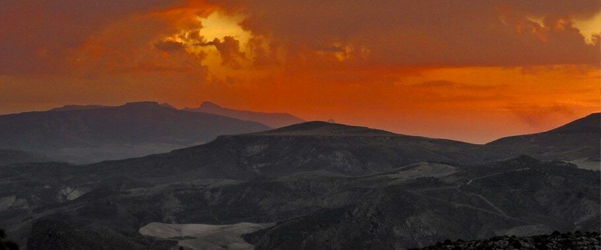 Una puesta de sol sobre una cadena montañosa con un cielo rojo