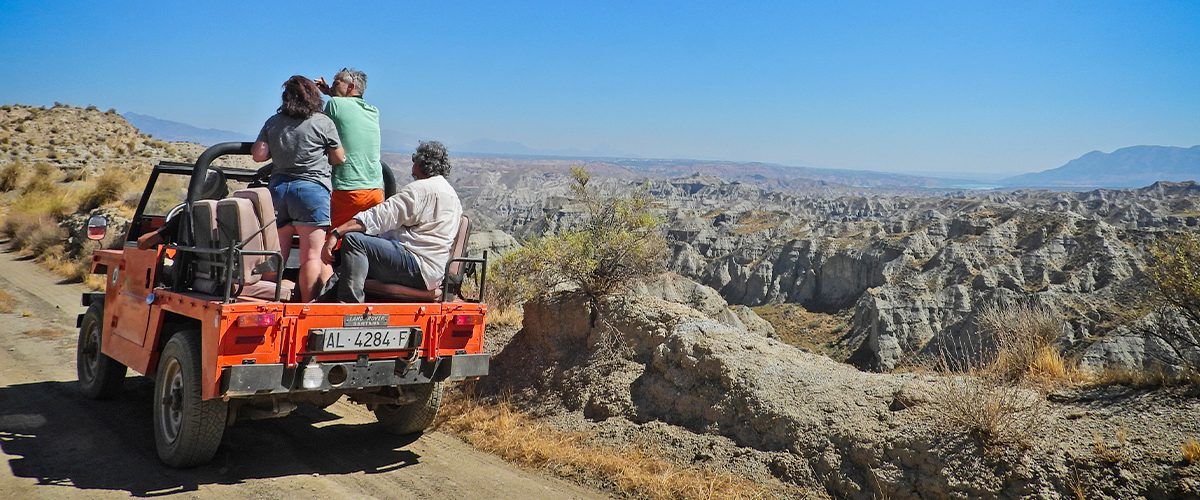 Un grupo de personas viaja en la parte trasera de un jeep por un camino de tierra.