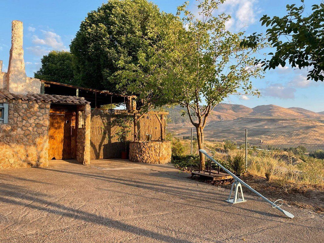 Un edificio de piedra con un árbol delante y montañas al fondo.