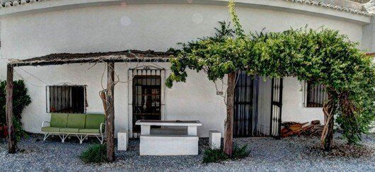 Una casa blanca con un porche con una mesa y sillas debajo de un árbol.