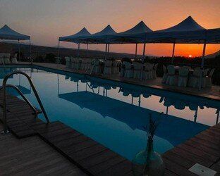 Una piscina rodeada de carpas y sillas al atardecer.