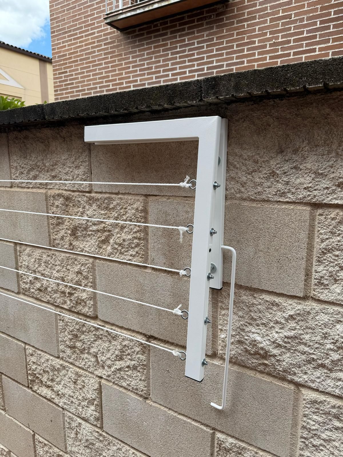 Un tendedero blanco está fijado a una pared de ladrillos.