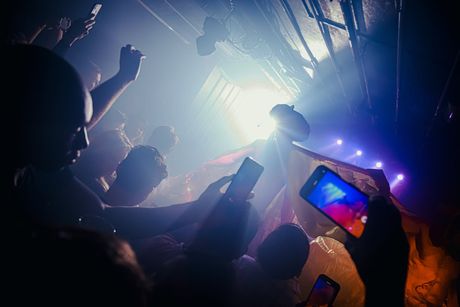 Multitud bailando en una discoteca oscura, con las manos en alto bajo luces azules y moradas de escenario
