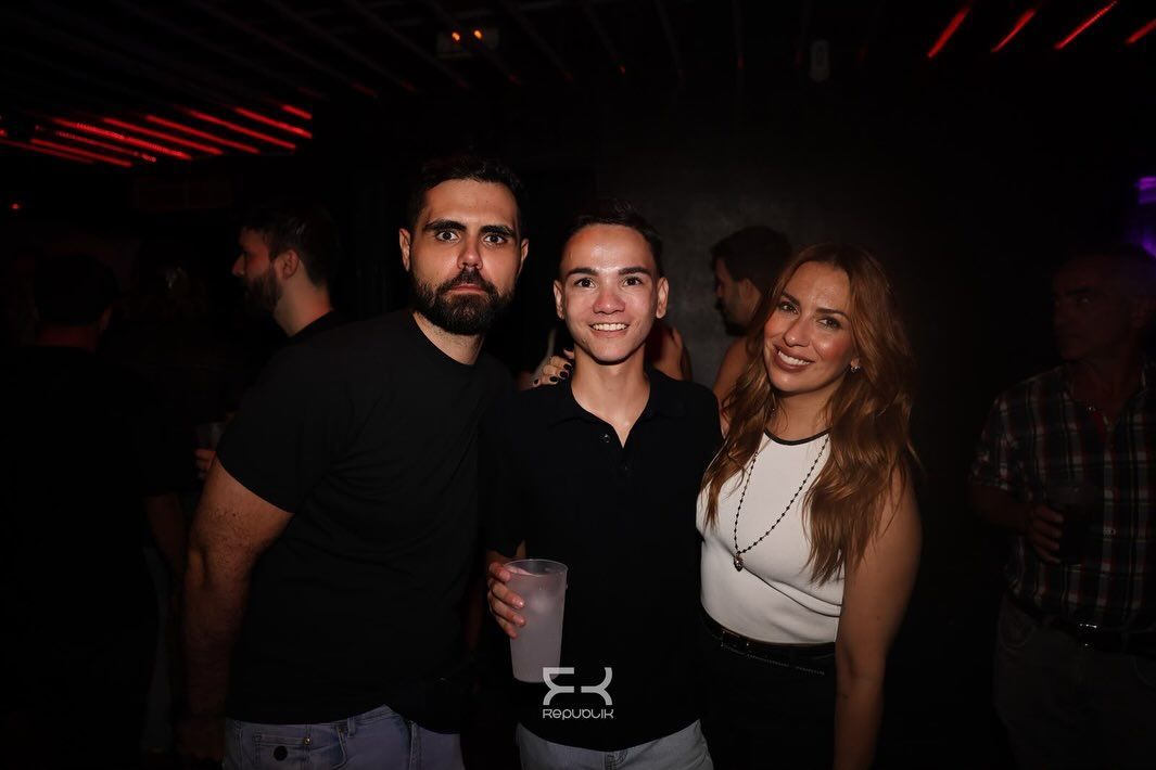 Tres personas posando juntas en una discoteca oscura, sonriendo a la cámara.