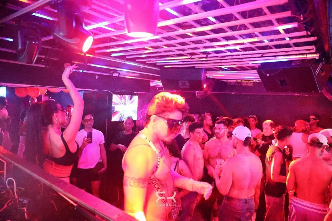 Discoteca abarrotada, con gente bailando bajo luces de neón rosas y moradas