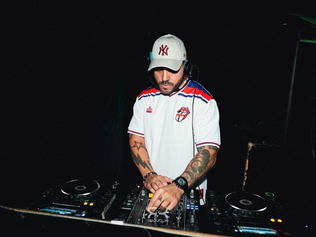DJ con gorra blanca y camiseta, mezclando en una mesa de DJ en una discoteca oscura