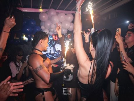 Personas bailando en una discoteca con las manos en alto, bebidas y luces brillantes en el escenario