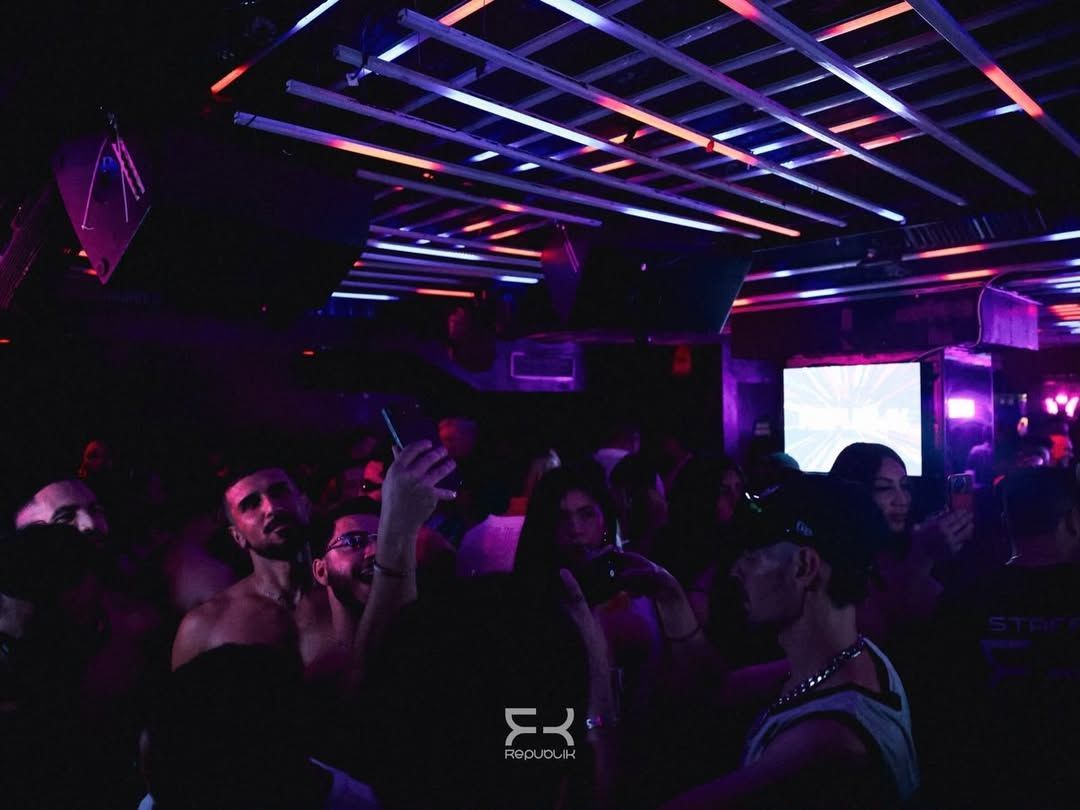 Discoteca abarrotada, con gente bailando bajo luces de neón moradas y azules