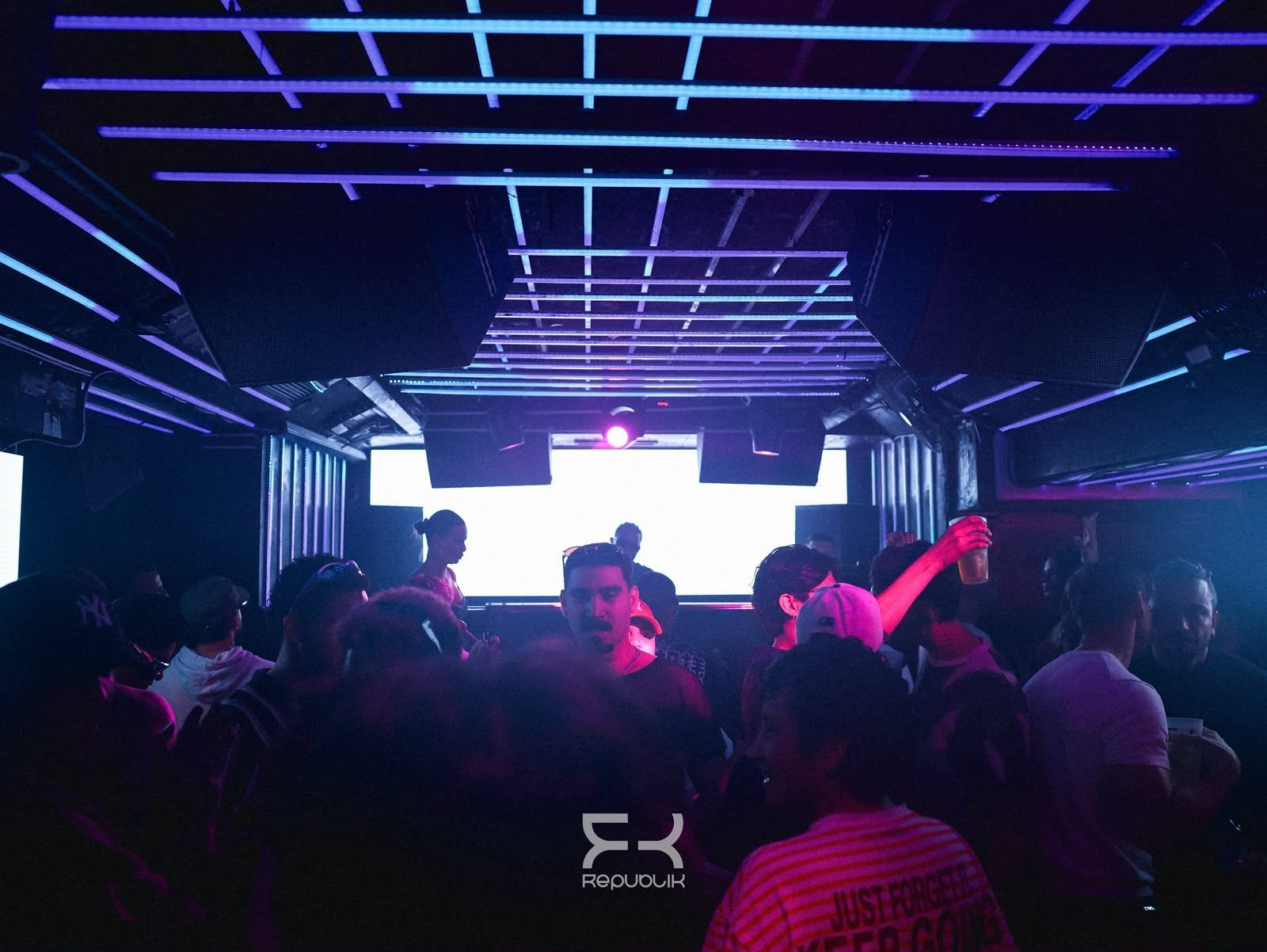 Discoteca abarrotada, con luces de neón moradas y un escenario de DJ muy iluminado al fondo