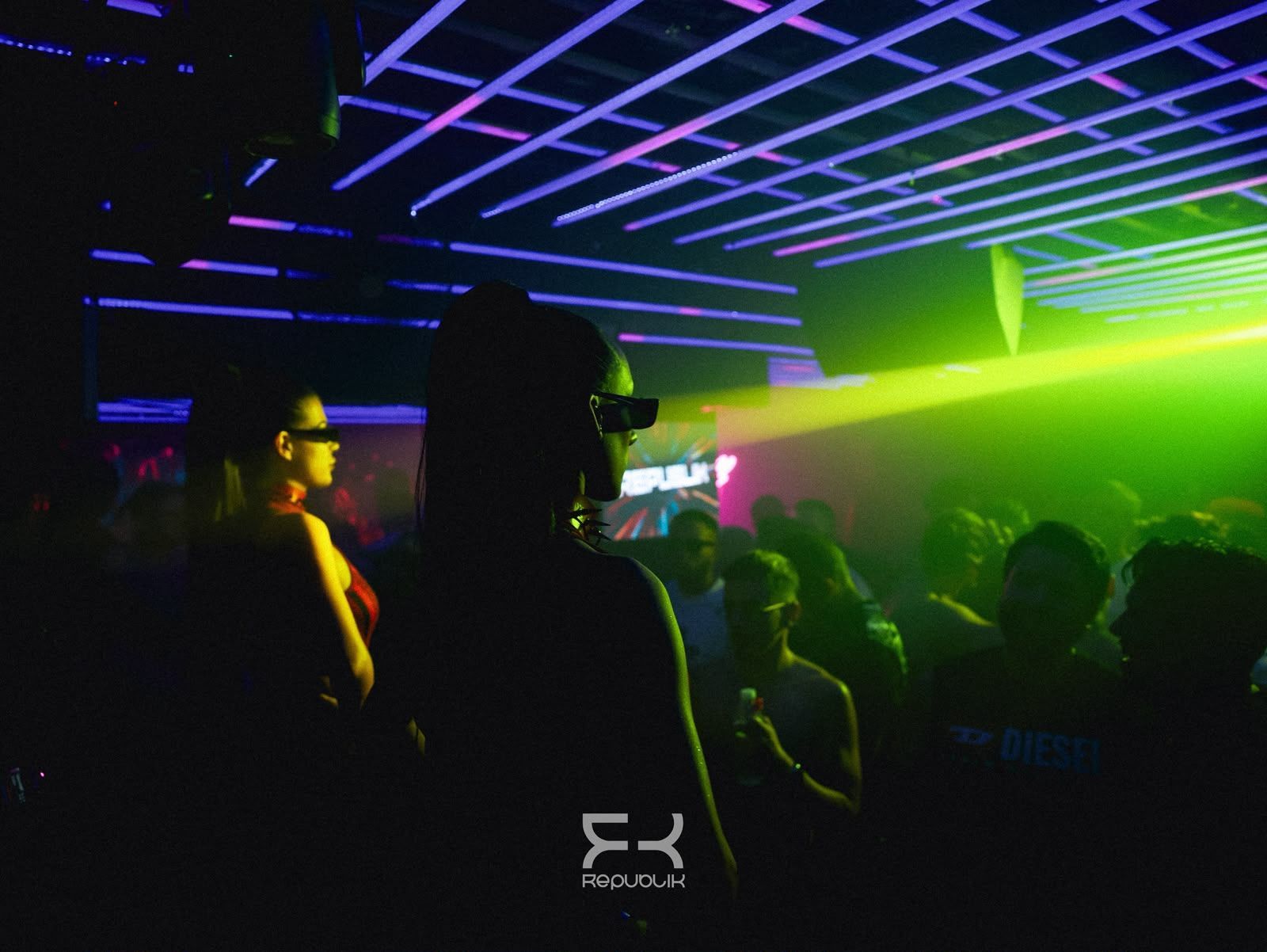Discoteca abarrotada, con luces de neón en el techo y un láser verde brillante sobre la pista de baile