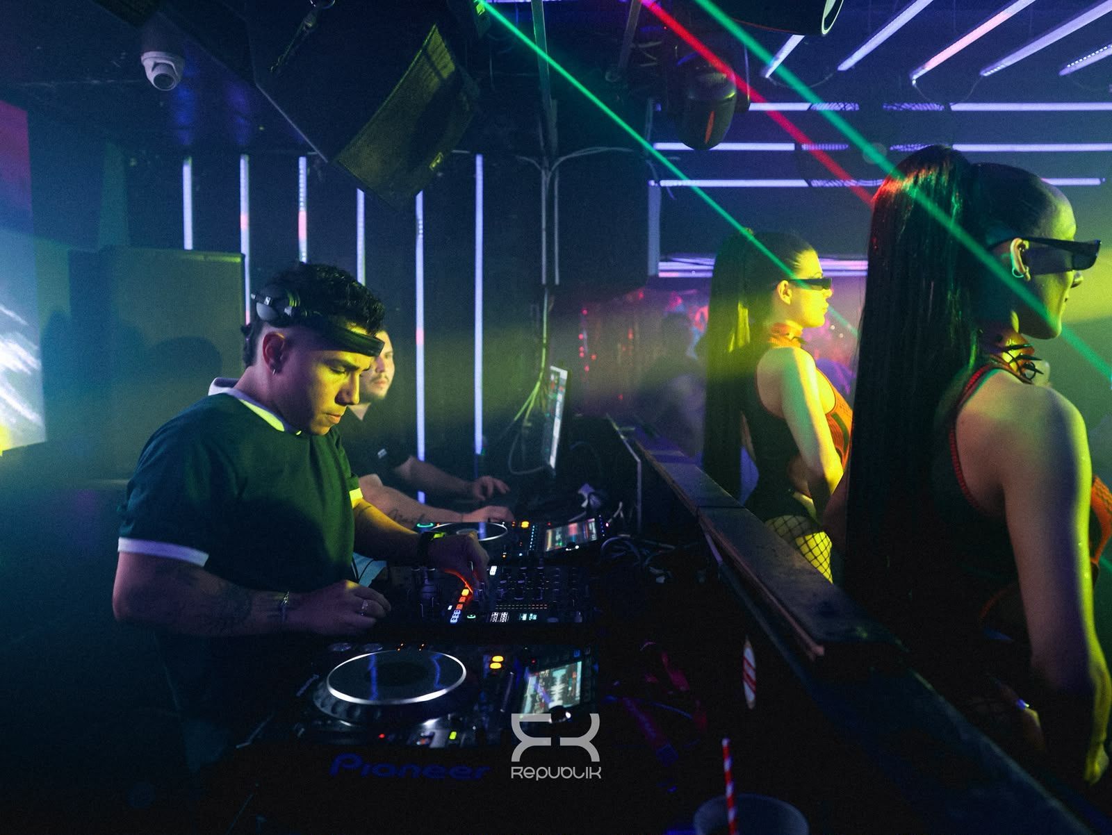 DJ actuando en una discoteca iluminada con neones, luces láser de colores y una multitud