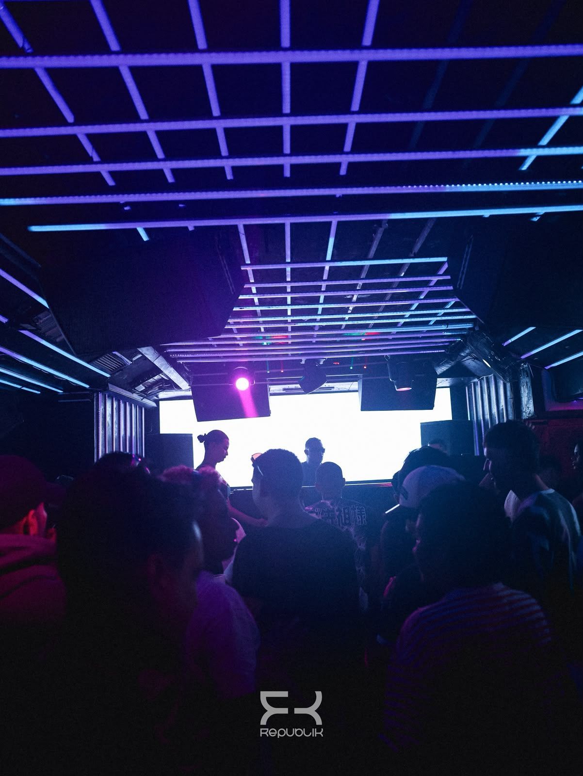 Discoteca abarrotada, con luces de neón moradas en el techo y un escenario blanco brillante al fondo