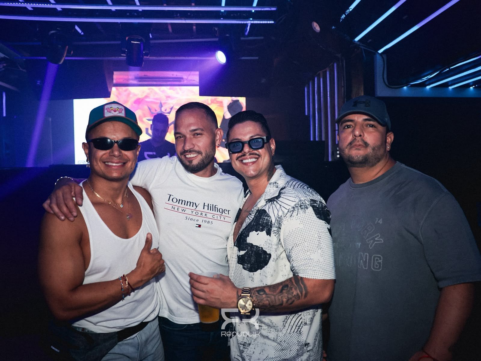 Cuatro personas sonríen juntas en una discoteca iluminada con luces de neón, posando con bebidas.