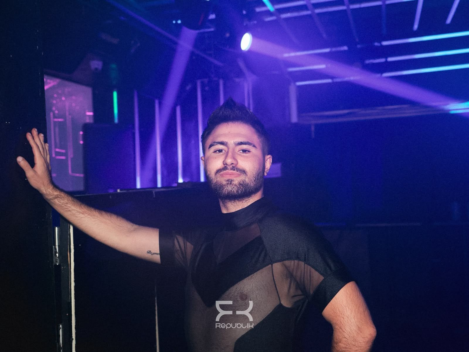 Persona posando con el brazo en alto bajo luces moradas de escenario en un ambiente parecido al de una discoteca