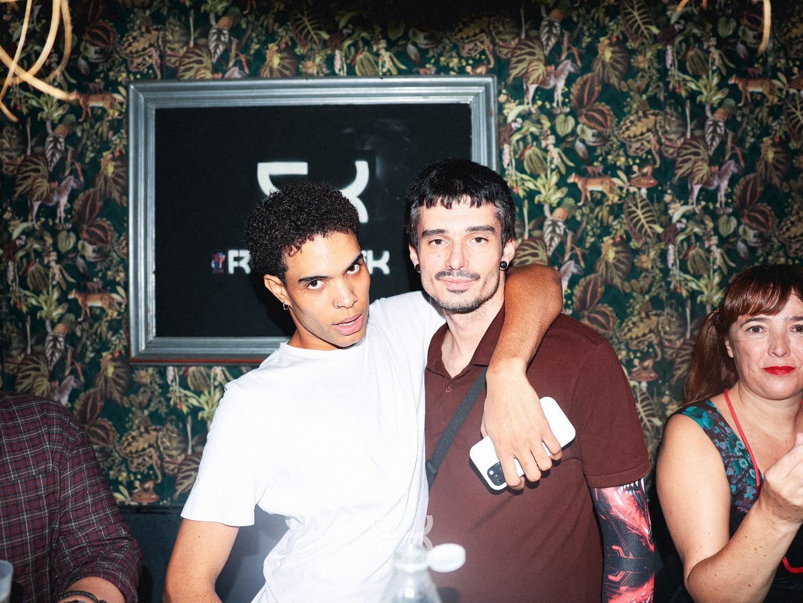 Cuatro amigos sonríen y posan juntos en una fiesta con poca luz y luces moradas de fondo.