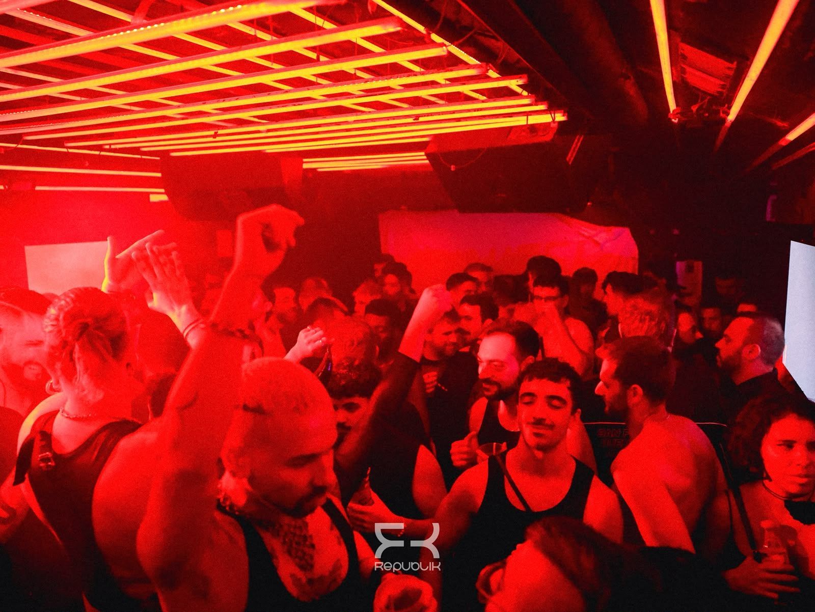 Discoteca abarrotada, con gente bailando bajo luces de neón rojas y brillantes en el techo