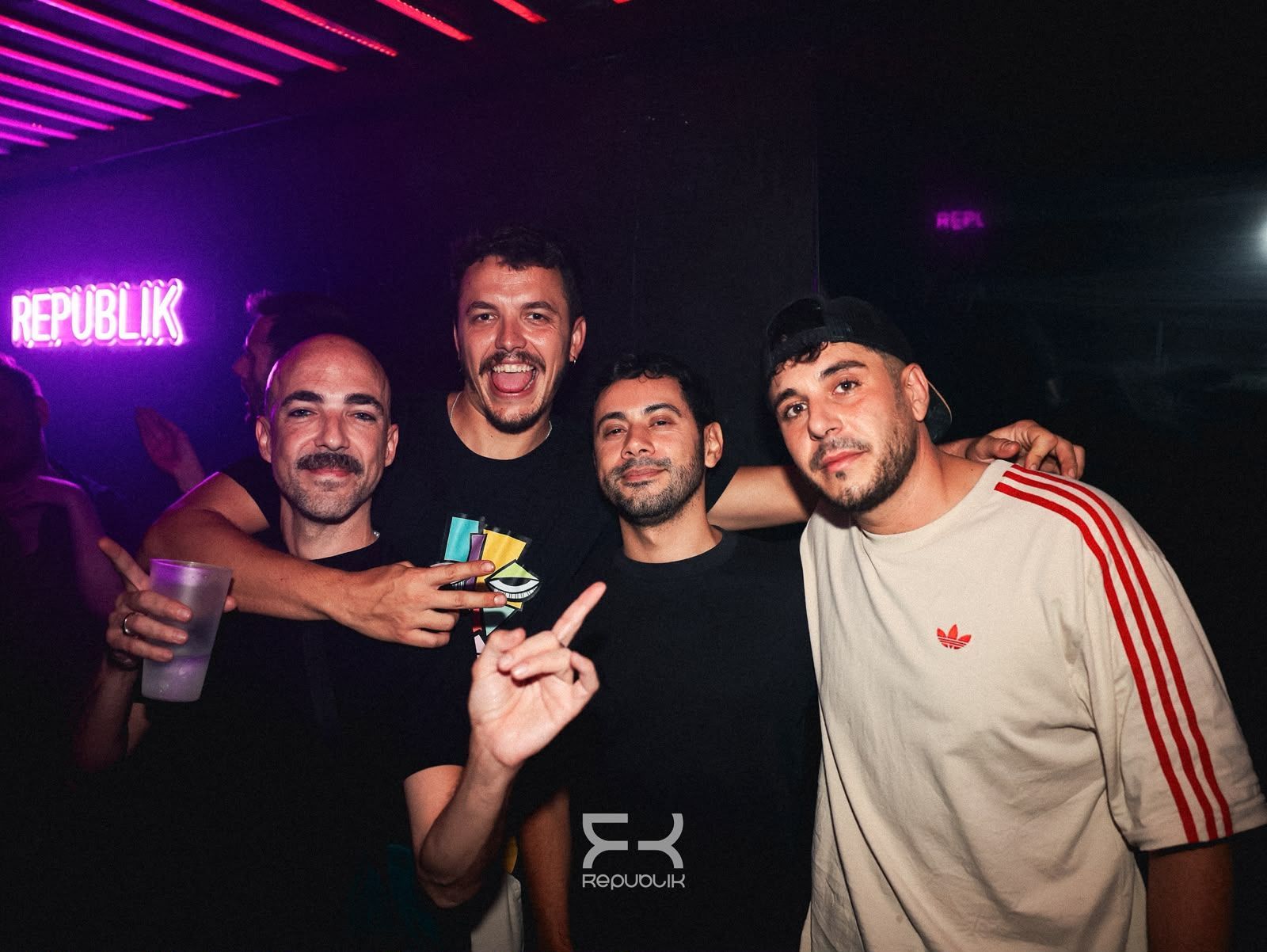 Cuatro personas posando en una discoteca con poca luz y luces de neón moradas; una de ellas sostiene una bebida.