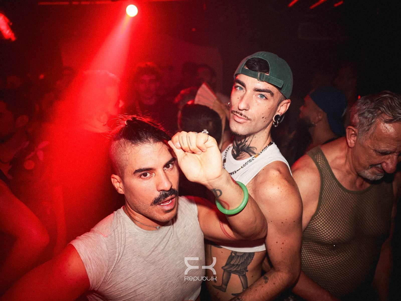 Personas bailando en una discoteca iluminada de rojo, un hombre alzando el puño hacia la cámara.