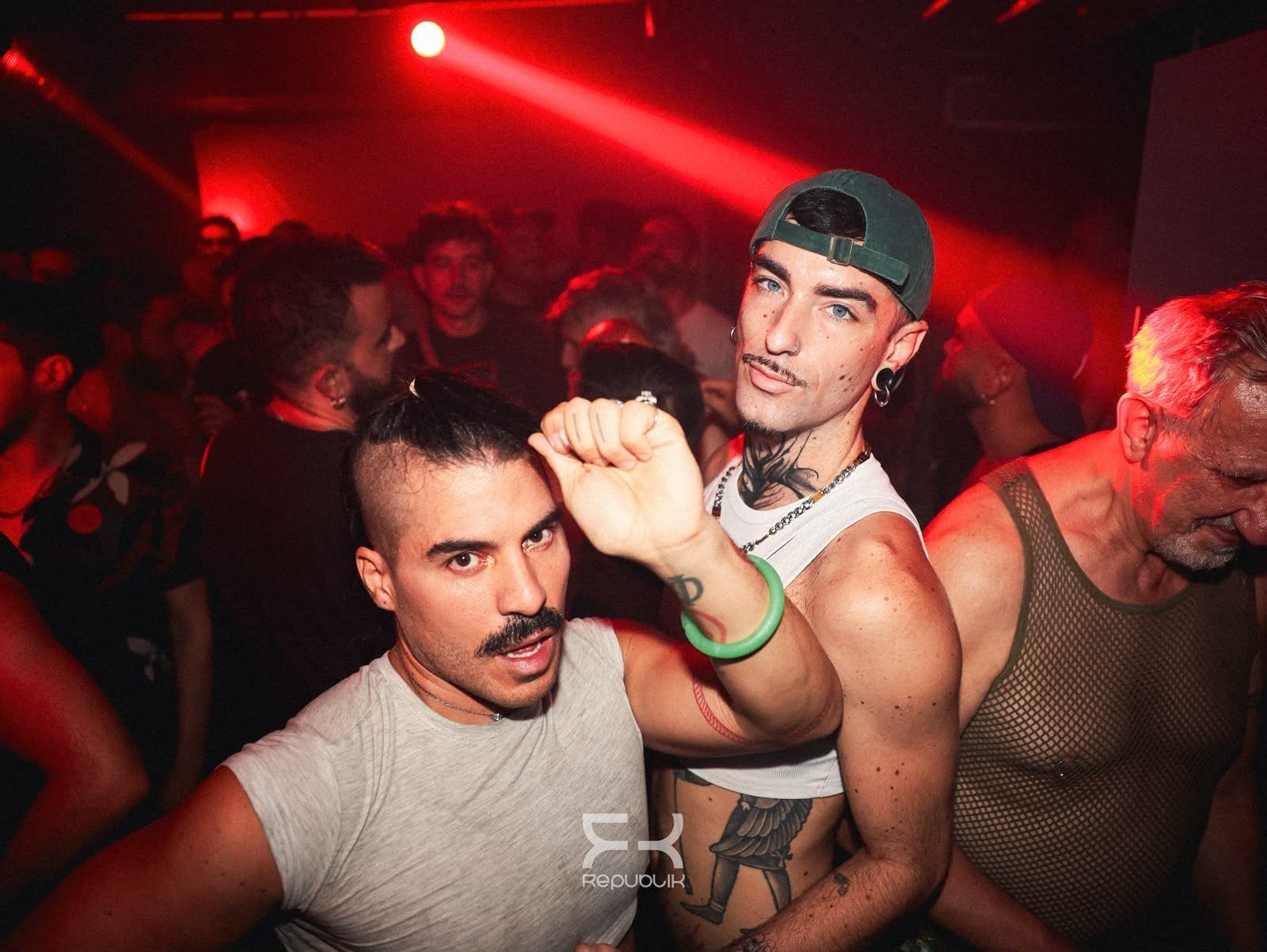 Tres personas bailando en una discoteca iluminada de rojo, una de ellas con el puño en alto hacia la cámara.