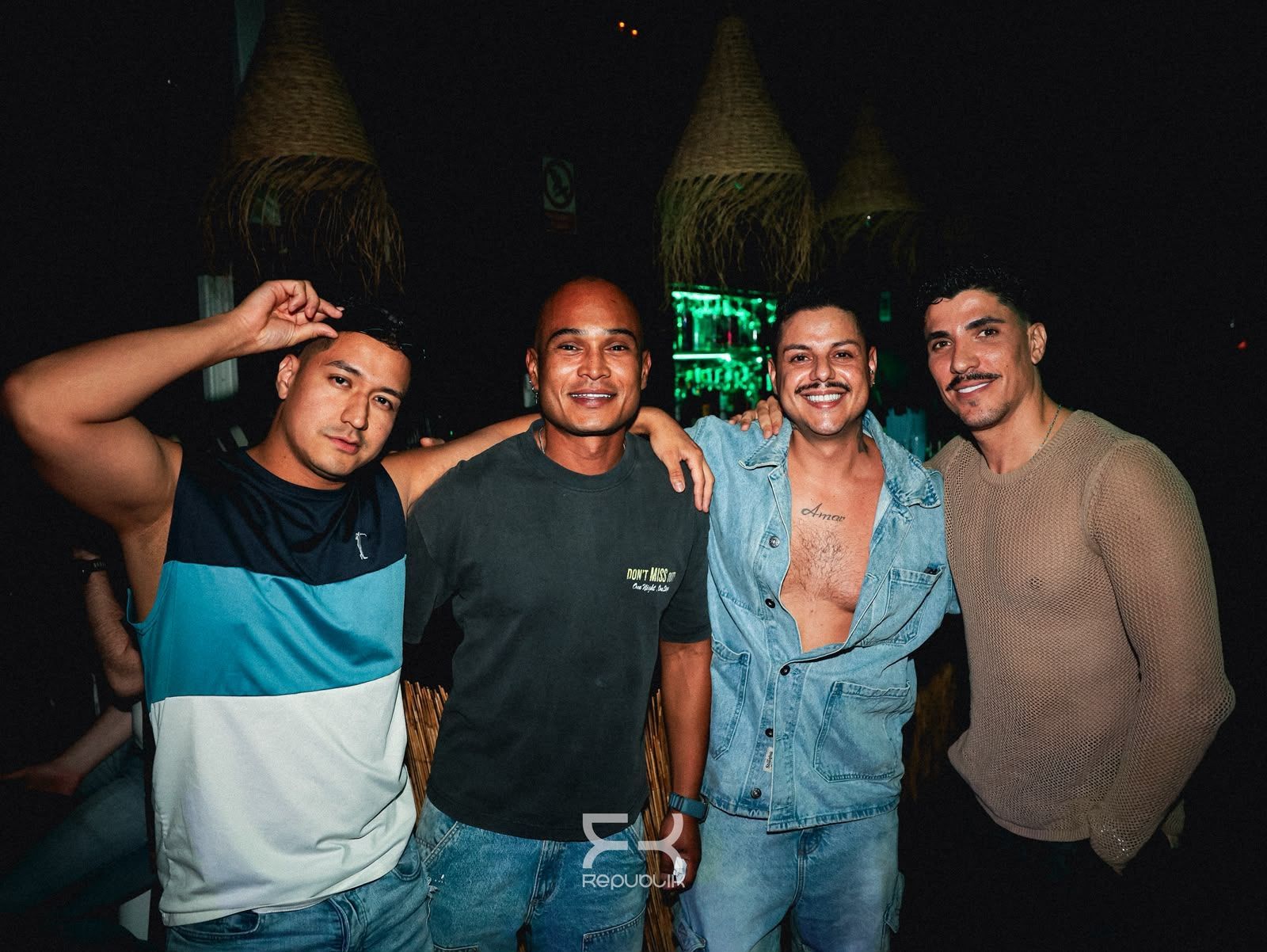 Cuatro amigos posan de noche, sonriendo y abrazados frente a unas luces brillantes.